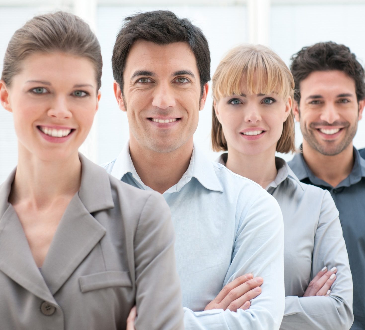 team Four professionally dressed individuals, smiling, standing in a line with arms crossed.