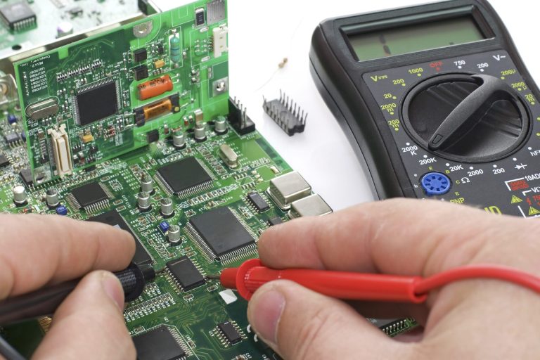electronic repair Hands testing a circuit board with a multimeter on a work surface.
